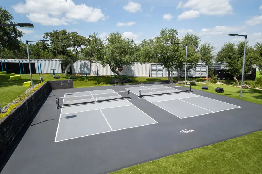 Two pickleball courts framed by oaks and light poles